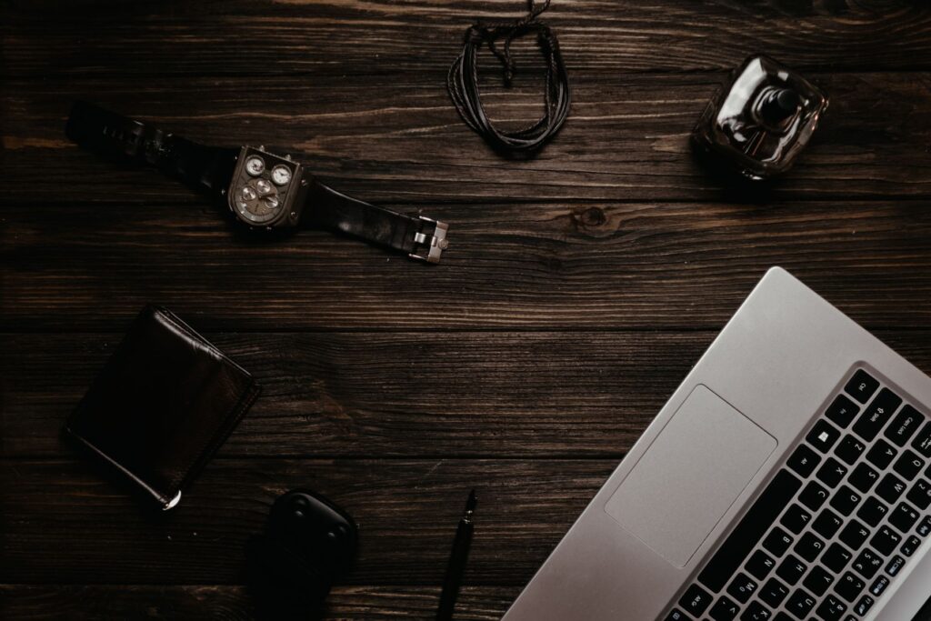 Flat lay of a laptop, watch, wallet and notebook on a dark wooden desk